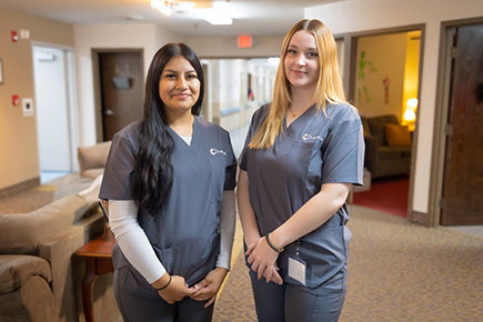 Two women in scrubs standing in a hallway.
